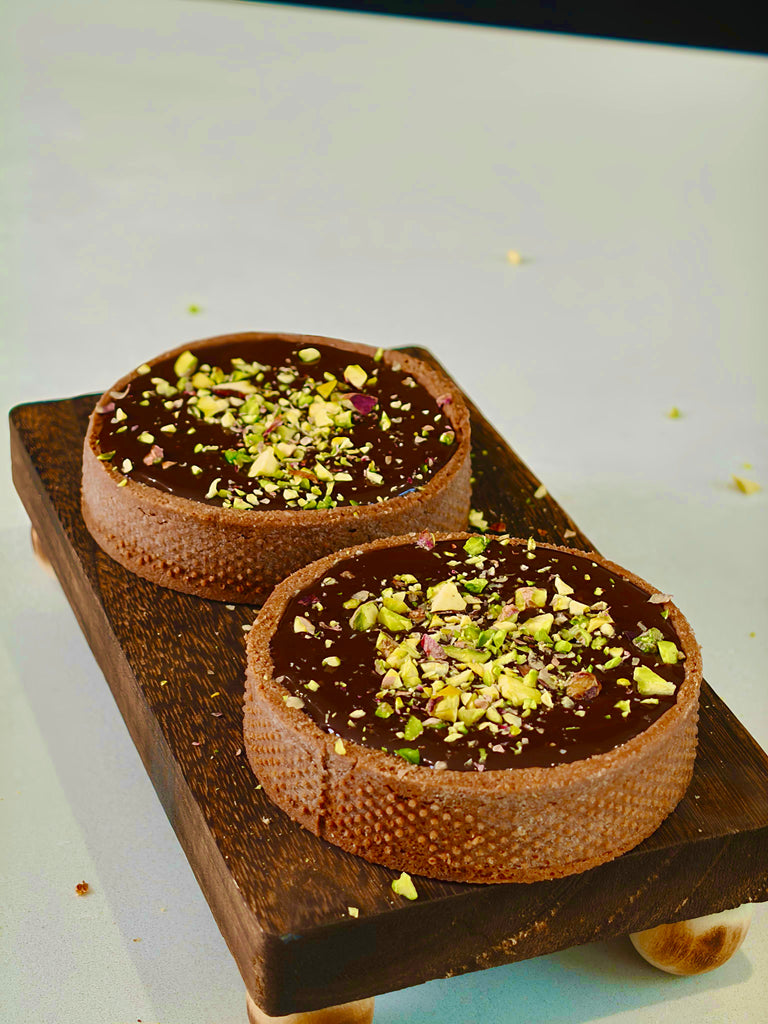 Two chocolate desserts with pistachio toppings on a wooden board.